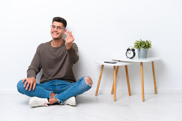 Young caucasian man sitting in his home isolated on white background making money gesture