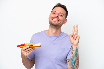 Young caucasian man holding sashimi isolated on white background smiling and showing victory sign