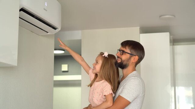 Happy family, father and little daughter fun turn on air conditioner using remote control. Cooler system
