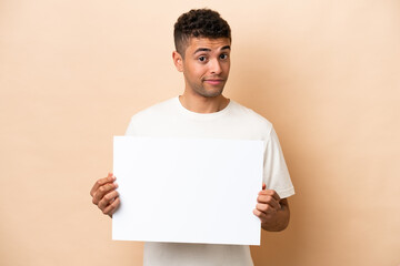 Young Brazilian man isolated on beige background holding an empty placard