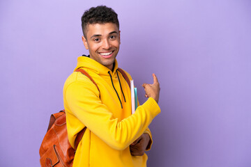 Young student Brazilian man isolated on purple background pointing back