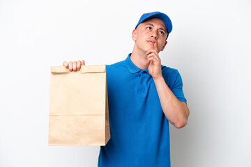 Young Brazilian man taking a bag of takeaway food isolated on white background having doubts while looking up