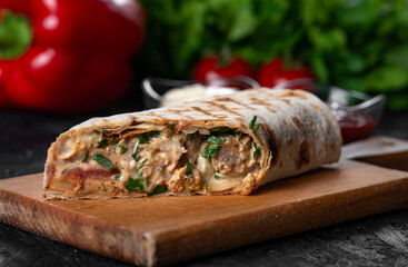 A delicious  doner kebab wrap with  meat, lettuce, tomato, onion and sauce on black background.