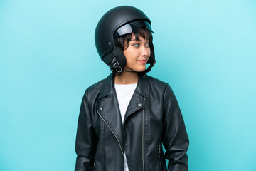 Young Argentinian woman with a motorcycle helmet isolated on blue background looking to the side and smiling