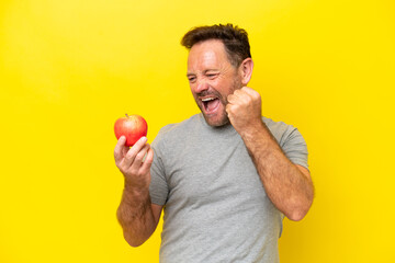 Middle age caucasian man with an apple isolated on yellow background celebrating a victory