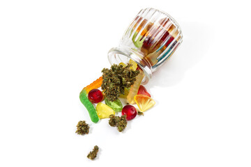 Various gummies and dried medical marijuana buds fell out of the embossed glass jar.  On a white background.  Lots of empty space, top view