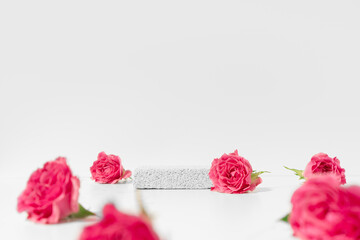 Cosmetics product presentation scene made with pumice stone pedestal and pink roses on white...