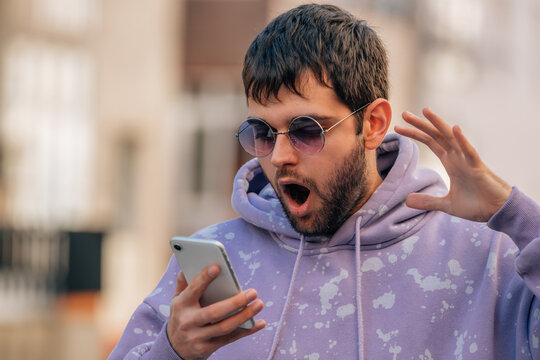 young man with sunglasses in the street with mobile phone with expression of amazement or surprise