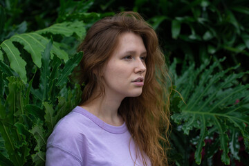 Portrait of young woman standing on an ivy, fern wall or in greenery, breathing, smiling and looking away girl relaxing outdoors at summer day.Love for nature, eco life,green leaves, green park