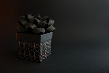 A black gift box with a geometric pattern and a black bow on a black background. Minimalist background for a holiday