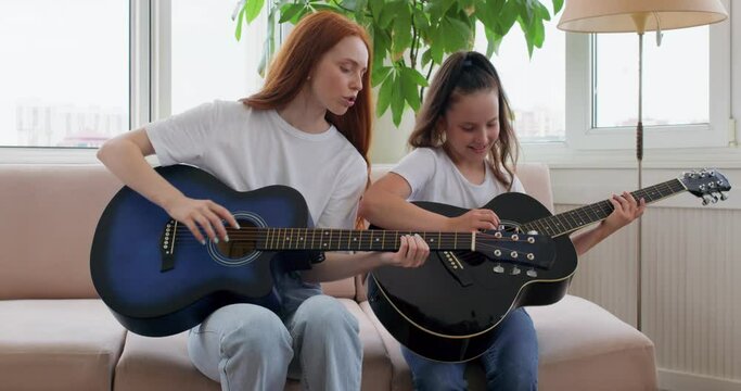 cheefrul mother and daughter sitting on couch playing guitar. self isolation quality family time at home together during coronavirus covid 19 pandemic.motherhood, childhood parenthood slow motion