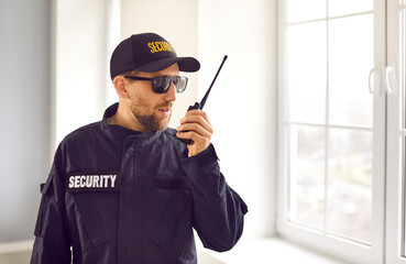 Guardian man in safety guard staff uniform hat and jacket with SECURITY text standing inside house,...