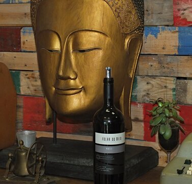 A noble wine bottle in front of a wooden Asian mask