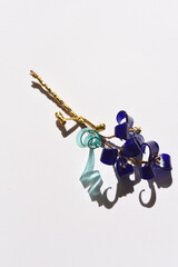 A glass flower twig, three blue flowers with golden stamens, and a blue transparent leaf, tied with a golden rope.