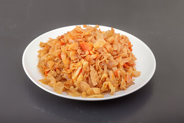 Stewed cabbage - bigos in a white porcelain plate on a dark table. Close-up