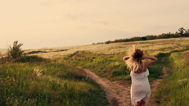 Beauty Girl Outdoors enjoying nature. Beautiful Teenage Model girl in white dress running on the Spring Field, Sun Light.