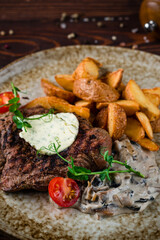 Beef steak with mushroom sauce, potato wedges, tomatoes and green peas, closeup.