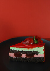 a piece of delicious sweet beautiful bright cake with strawberries on a black kitchen plate and a red background and decorated with pink berries around