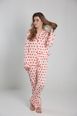 beautiful blonde girl on a white background in pajamas. pajamas with hearts. romantic pajamas. Valentine's Day. studio photo shoot in satin pajamas with a heart print. clothes for sleep and home