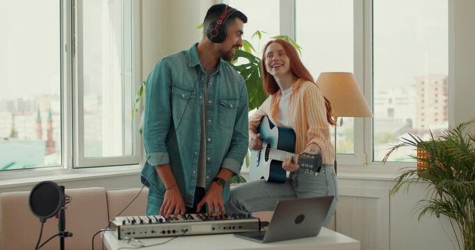 Happy bearded talented man playing piano, red-haired woman playing guitar at home, singing songs, having fun at studio. lifestyle, free spare time, hobby, interests, slow motion,music lovers