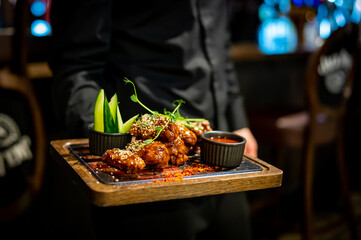 Waiter hold plate with fried chicken wings in restaurant or pub