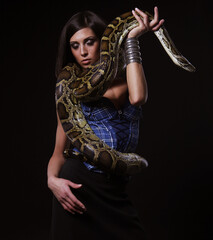 sexy brunette woman holding python over black background