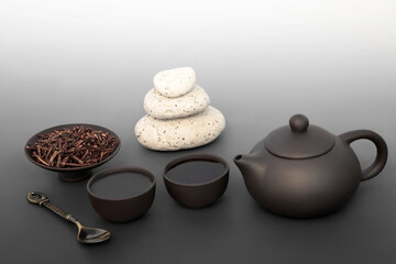 Obraz na płótnie Canvas Japanese kuchika tea ceremony for balance with pebble stack, ceramic tea set. Zen spiritual mindfulness harmony concept on gradient grey. Healthy asian culture drink.