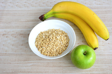 A bowl of oat flakes with a green apple and bunch of yellow bananas, close-up