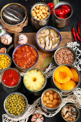 Canned vegetables, beans, fish and fruits in tin cans on black background. Food stocks.