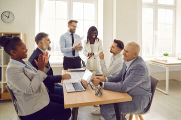 Diverse corporate business team having fun during a work meeting. Group of happy young and senior multiethnic people sitting at an office table and laughing at something funny