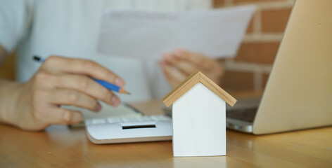 close up house model with man hand press on calculator to check and summary expense of home loan mortgage for refinance plan , people lifestyle concept