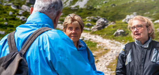 Elderly people relaxing at the end of a mountain hike, talking along the alpin trail.