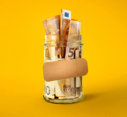 Euro bills in glass jar with blank sticker on yellow background. Saving money concept