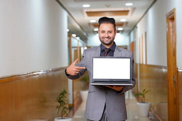 Indian businessman showing blank laptop screen.