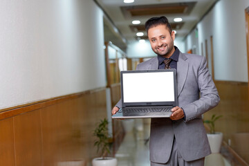 Indian businessman showing blank laptop screen.