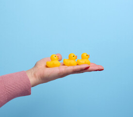 A woman's hand holds a yellow rubber duck on a blue background, a bath toy