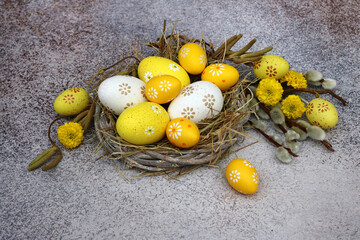 Osternest mit gelben und weißen Ostereiern mit Blumen und Zweigen dekoriert.