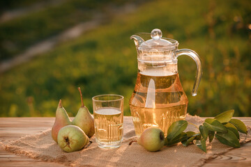 A glass with pear juice and basket with pears on wooden table with natural orchard background on...