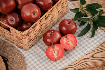 Fresh ripe red apples in the basket on wooden table with natural orchard background. Vegetarian fruit composition. Harvesting concept