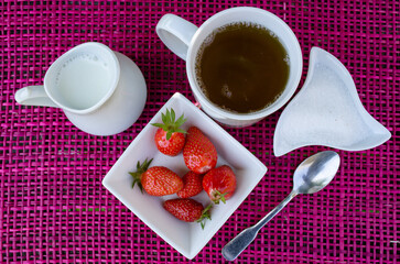 petit déjeuner, thé et fraise sur fond rose, un pichet de lait et du sucre blanc