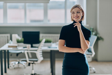 Fototapeta na wymiar Confident businesswoman looking away and smiling while standing in the office