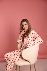 beautiful woman in pajamas with a heart print on a pink background is sitting on a chair. Pink...