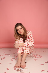 beautiful girl in heart print pajamas on a pink background. surprised look, Confetti. Pink pajamas with red hearts. clothes for sleep and home.