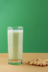 Organic non dairy pistachio milk in glass. Vegan pistachio milk and pistachios on a beige green background