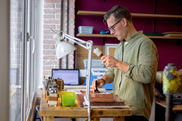 young skilled artisan in stylish green shirt working with Leather mauls.hobby, job, profession, occupation, close up side view shot
