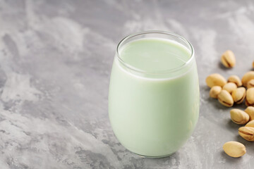 Homemade pistachio milk in a low glass on concrete. Organic pistachio milk and pistachios on a gray background. Copy space