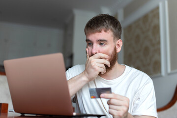 Nervous sad upset confused young man, stressed worried guy having problem with paying, buying online, payments with credit blocked bank card, looking at screen, monitor of laptop. Internet fraud