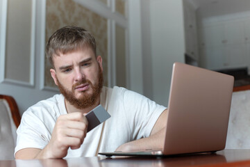 Nervous sad upset confused young man, stressed worried guy having problem with paying, buying online, payments with credit blocked bank card, looking at screen, monitor of laptop. Internet fraud