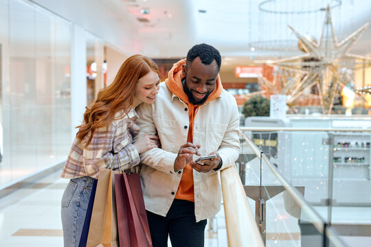 young people Using Cellphone Holding Colorful Shopper Bags Standing In Mall Happy Customers Using Application Purchasing Clothes Online Smartphone. Ecommerce Shopaholism. happiness. free spare time