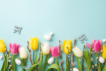 Easter concept. Top view photo of easter eggs colorful tulips pussy willow and butterflies on isolated pastel blue background with empty space